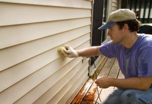 Man washing vinyl siding by hand with brush