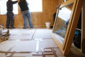 workers installing wood window with new window in foreground