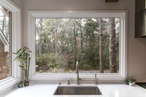 A picture window at a sink shows a forest with green trees in a Naperville home.